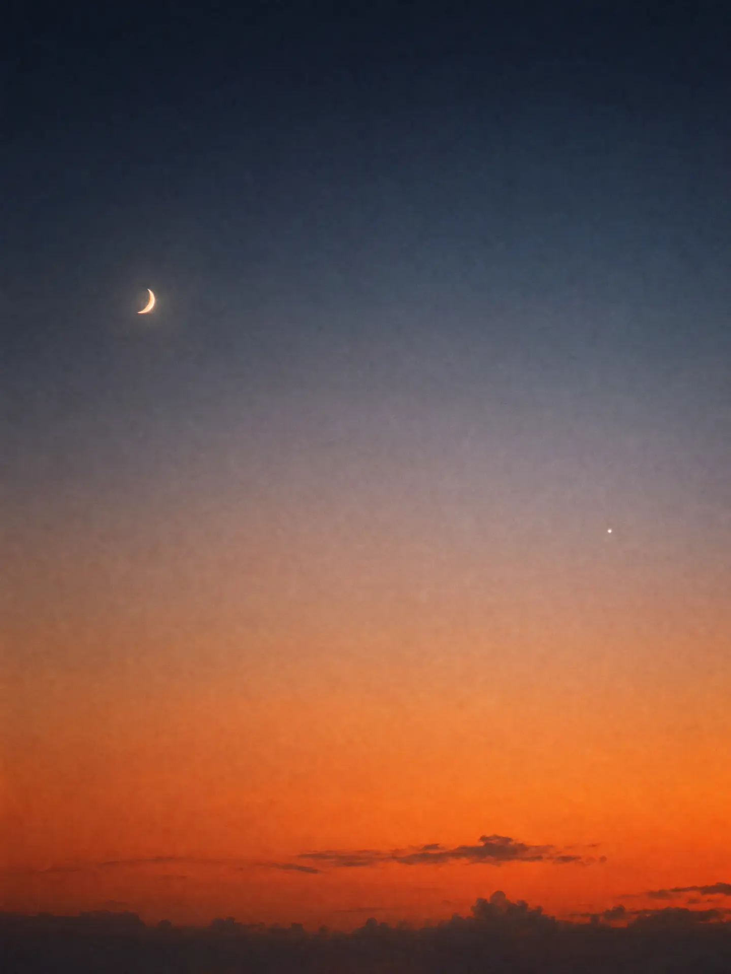 A crescent moon and bright star above an orange dusk horizon